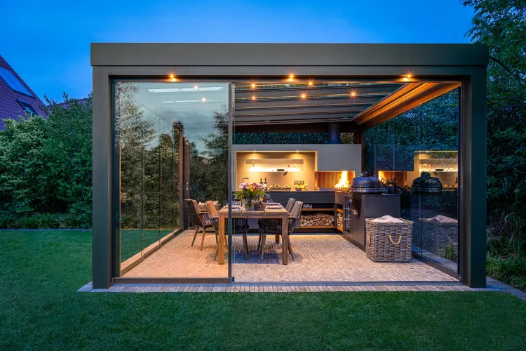 Verglaster Outdoor-Pavillon mit integrierter Küche, Esstisch und Feuerstelle in der Dämmerung