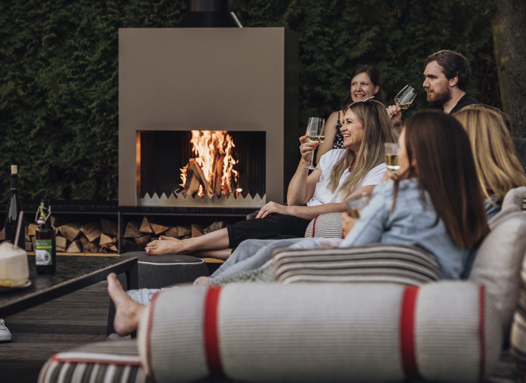 Outdoor Wohnzimmer mit moderner Feuerstelle, stilvollen Loungemöbeln und stimmungsvoller Beleuchtung bei Sonnenuntergang