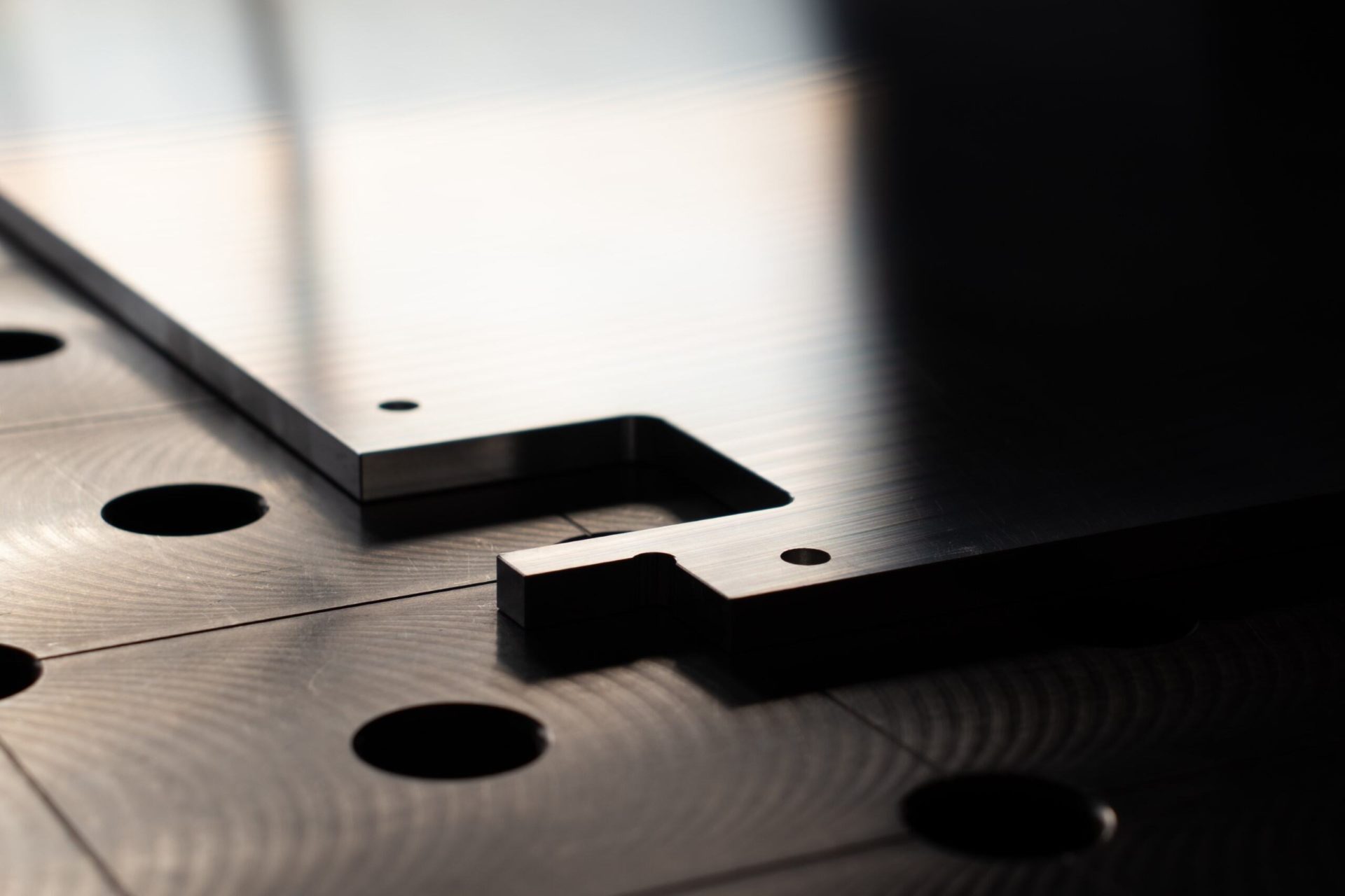 Detailaufnahme einer gefrästen Aluminiumplatte mit Bohrlöchern auf strukturierter Arbeitsfläche