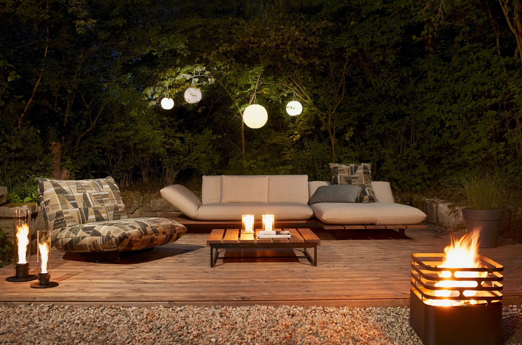 Outdoor Wohnzimmer mit moderner Feuerstelle, Loungemöbeln und stimmungsvoller Beleuchtung in einem stilvollen Garten