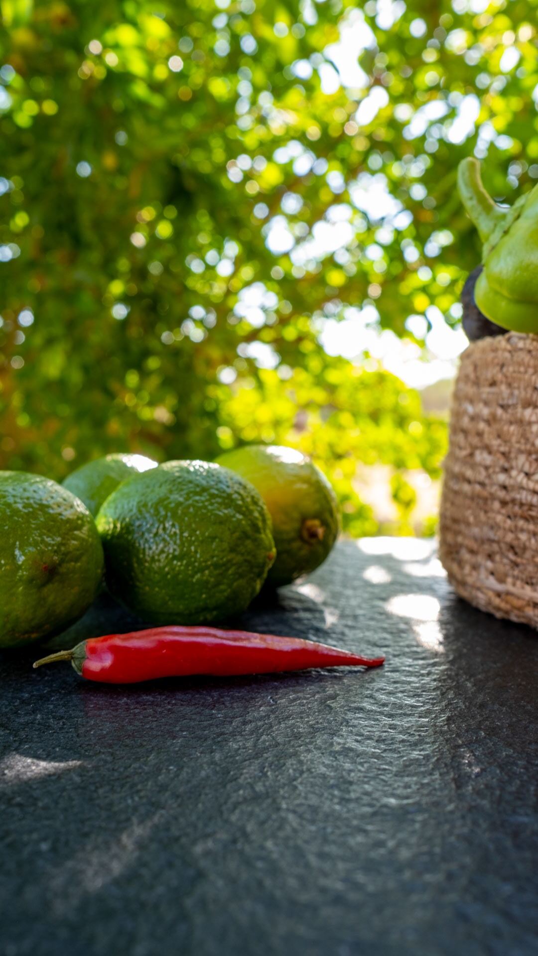 Frische Limetten und rote Chili auf schwarzer Steinplatte mit mediterraner Lichtstimmung im Hintergrund